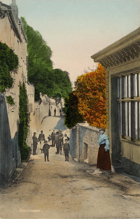 Around 1900  Cliff Road, Salcombe, at Baker's Well, view from the southern end. Cliff House is at rear left. Children standing in road, young lady in doorway of house on right, which is now part of Salcombe Harbour