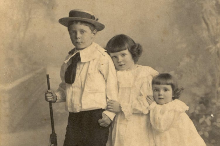 Portrait photo of three grandchildren of Thomas Weymouth, solicitor of Kingsbridge. Harold, Gladys and Evelyn Allin, children of Rev and Mrs Allin of Alleron, Loddiswell. Eldest child holding a gun.