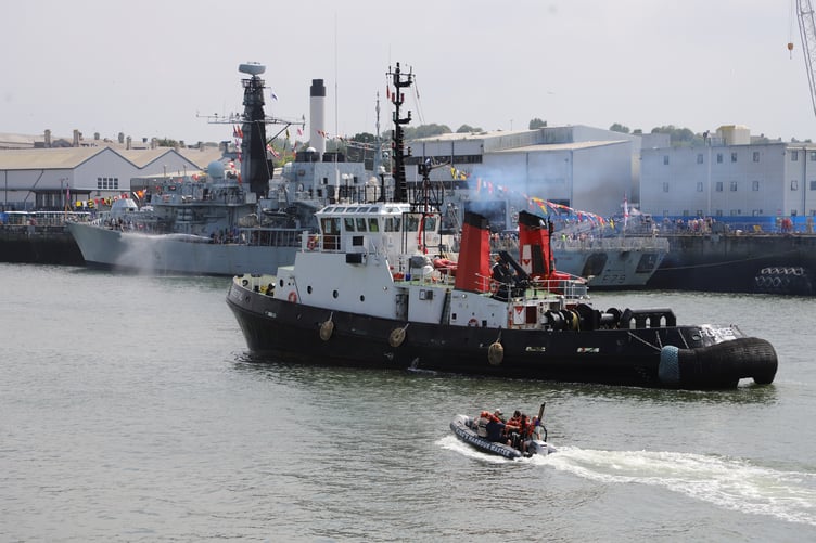 A tugboat steams past the frigate HMS Portland at Devonport Open Days which attracted thousands.